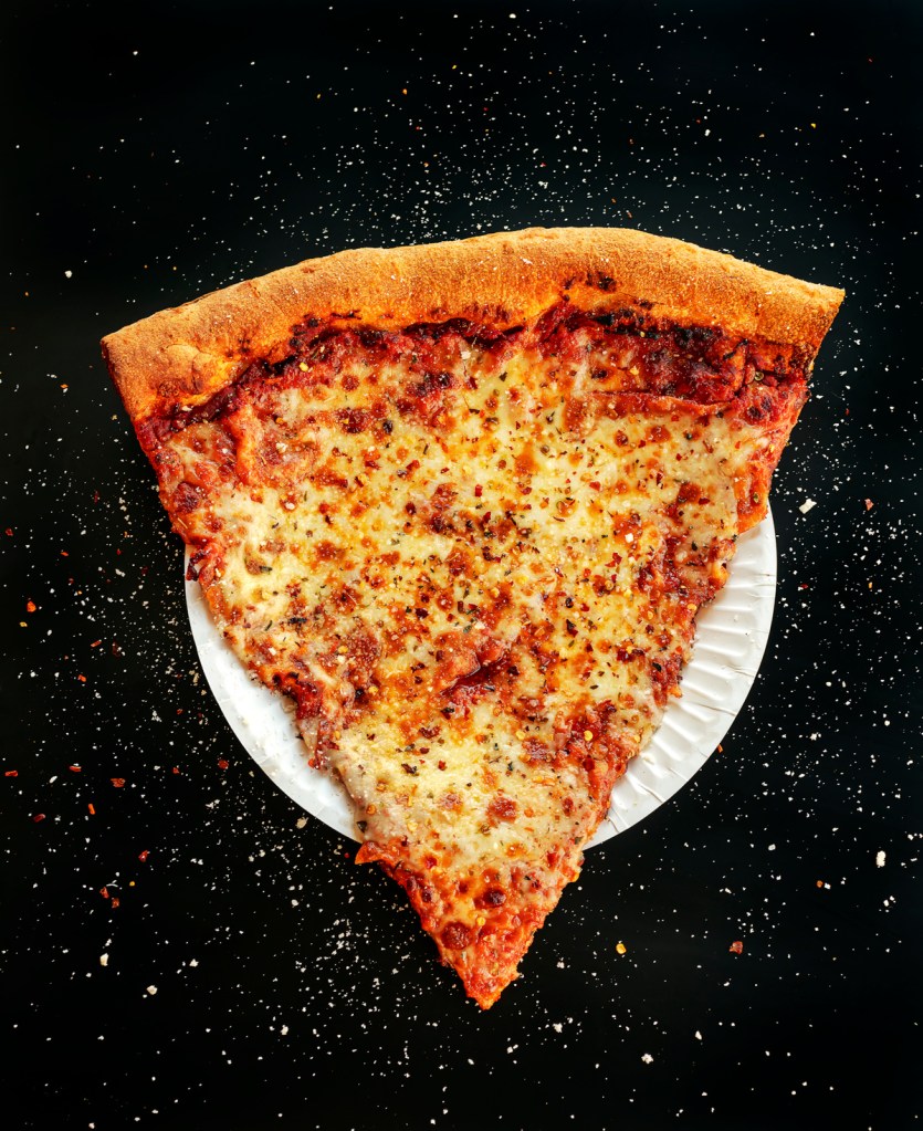 A single slice of pepperoni pizza on a white paper plate, set against a dark background with sprinkled spices.