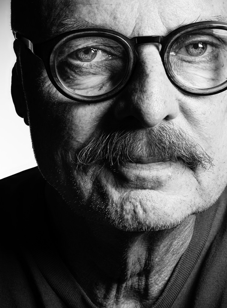 Close-up portrait of an older man with glasses and a mustache, featuring detailed facial textures in black and white.