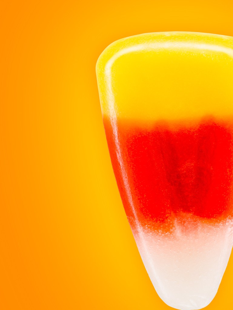 Close-up of a colorful layered ice pop featuring yellow, orange, red, and white sections against an orange background.